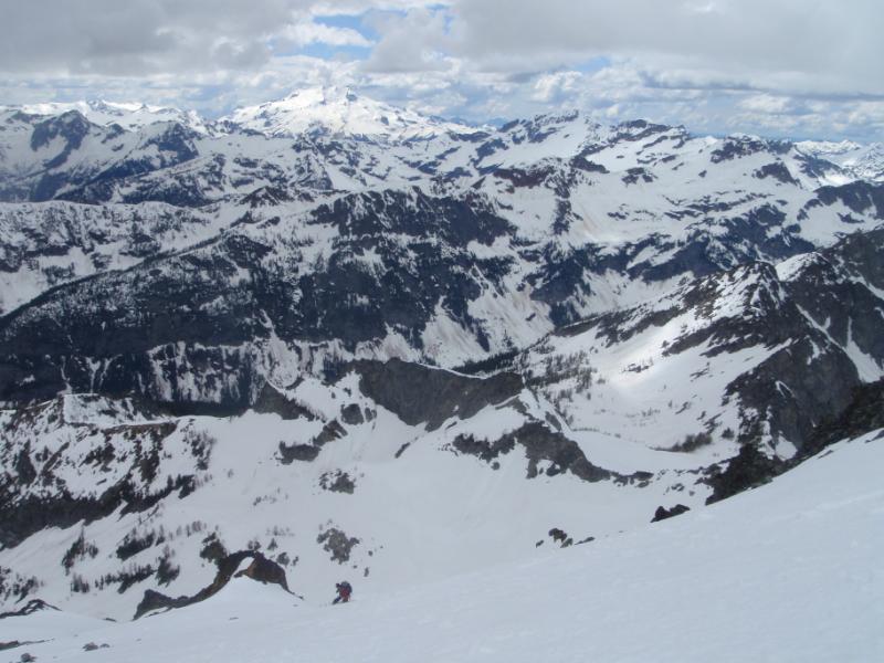 Snowboarding down while looking west towards Glacier Peak from the summit of Seven Fingered Jack