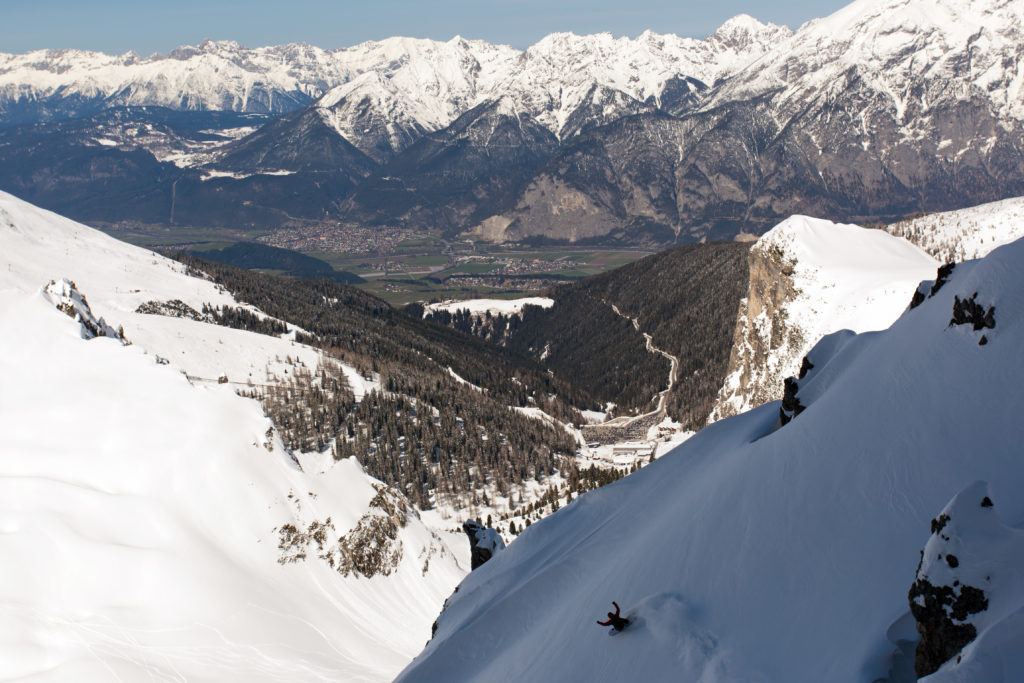 Making a snowboard turn on the sidewall in the Axamer Lizum backcountry with the Innsbruck mountains in the distance