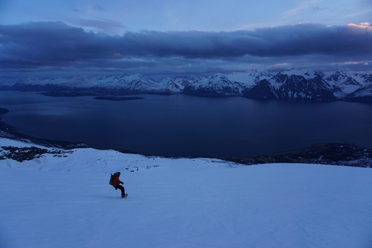 Snowboarding down Storhaugen with the Lyngen Alps of Norway in the distance