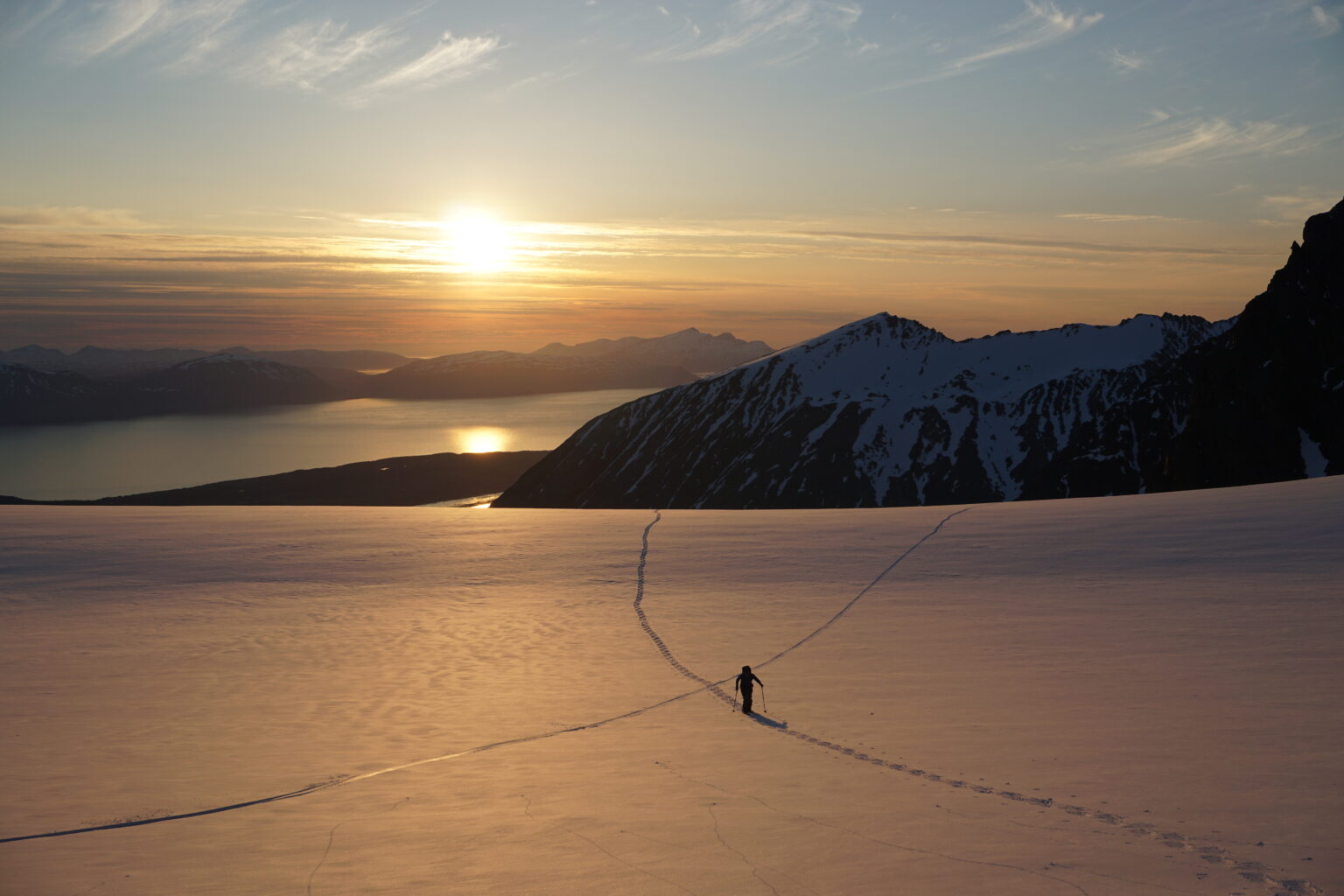 Ski touring up the Lenangsbreen Glacier in the Lyngen Alps of Norway as the Midnight sun sets to the North