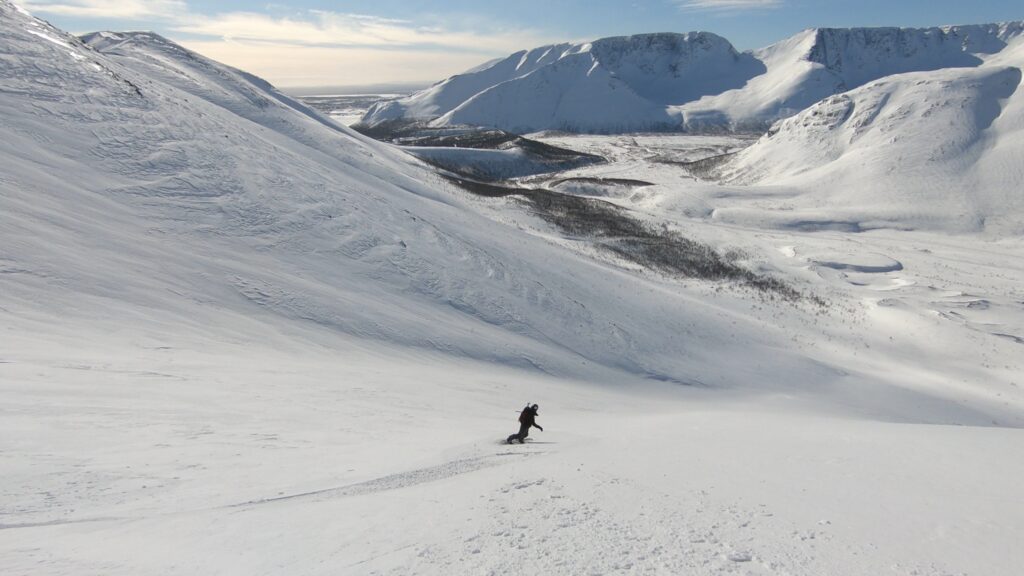 Snowboarding down the Kukisvumchorr Backcountry with the Khibiny Mountains in the background