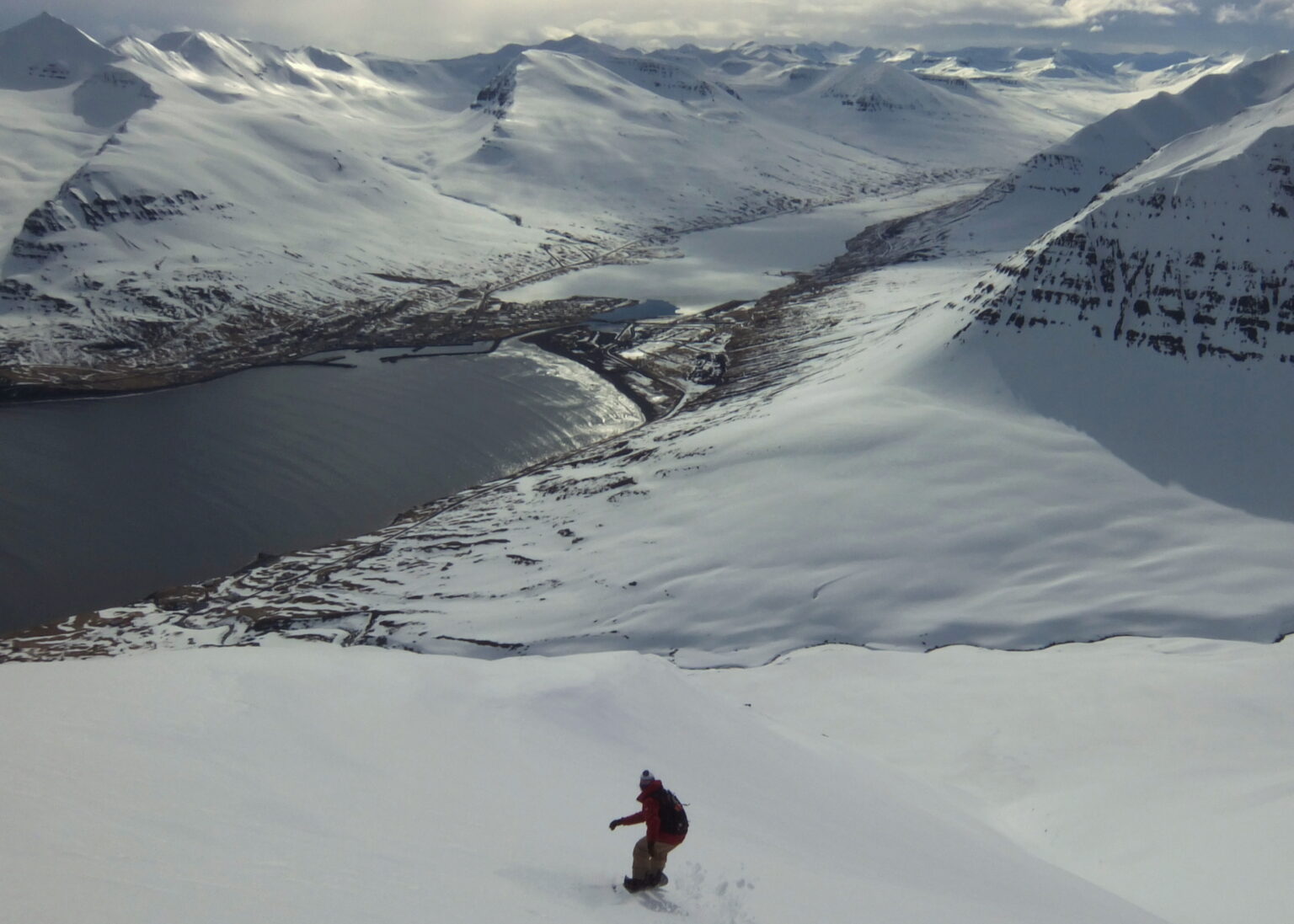 Snowboarding down from the summit of Arnfinnsfjall with Ólafsfjörður in the distance in Northern Iceland