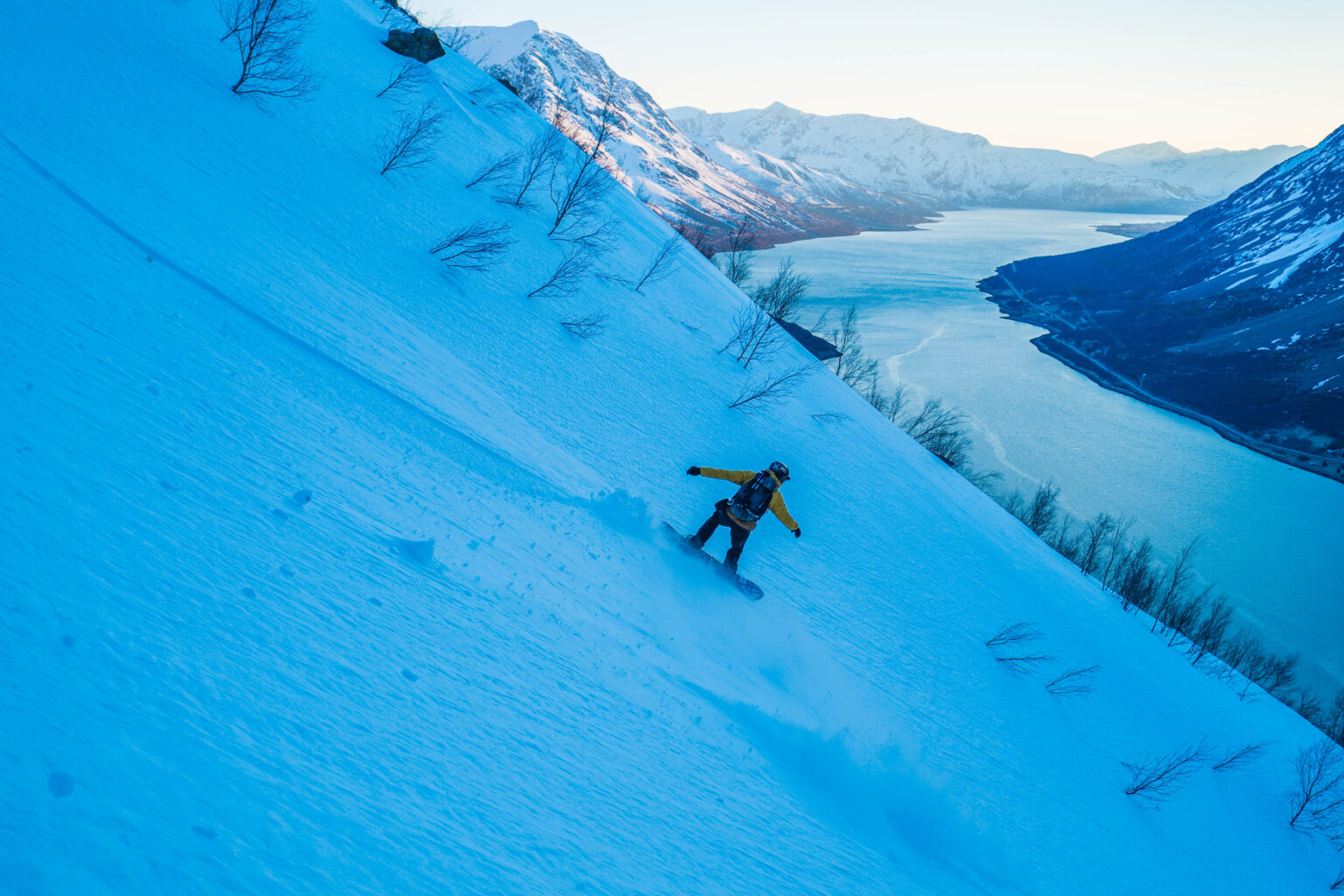 Snowboarding down the North Couloir of Rornestinden iwith the fjord in the background in the Lyngen Alps